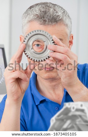 Vertical shot of an engineer gazing through a gear wheel at the camera during inspection indoors.