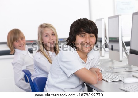 Smart students in computer class smiling at the camera while working on desktop computers