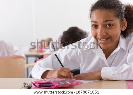 A confident school girl in white uniform under selective focus taking a test in front of a softly blurred background