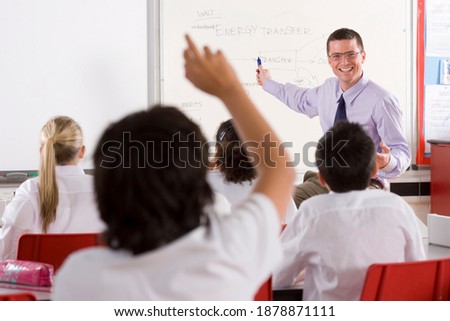 A wide shot of a smart smiling teacher explaining an interesting topic written on the whiteboard to a group of students in a classroom