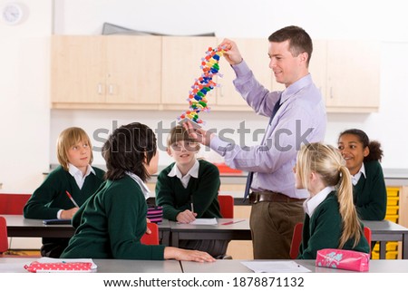 Wide angle shot of a classroom with Students sitting on their desks while watching the biology teacher demonstrate a 3D DNA model