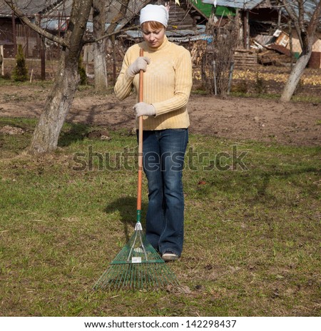 Gardening, agriculture concept - woman working with a rake cleaning dry leaves
