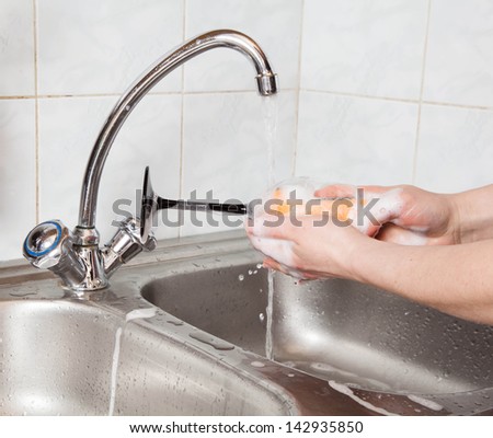 woman hands rinsing a wine glass under running water in the sink