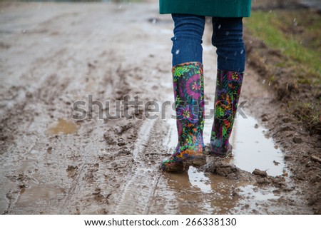Woman with rain boots jumps into a puddle