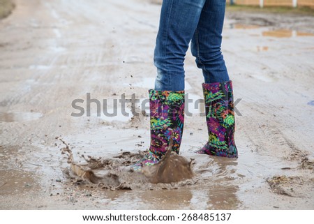 Woman with rain boots jumps into a puddle