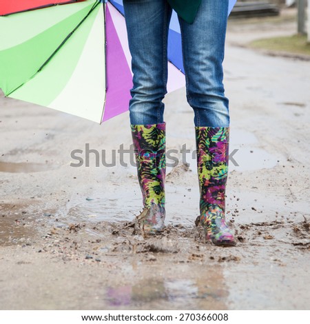 Woman in rain boots jumps into a puddle