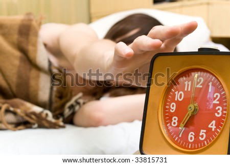 Young woman snoozing a red alarm clock