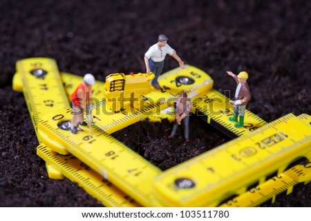 Tiny miniature maintenance team repairing a stylised road with hammer drill and compacting roller while one man works in a pit