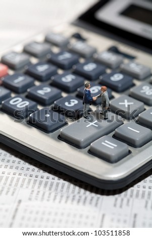 Miniature toy models of men standing on the keys of a calculator shaking hands on a business agreement or accounting deal