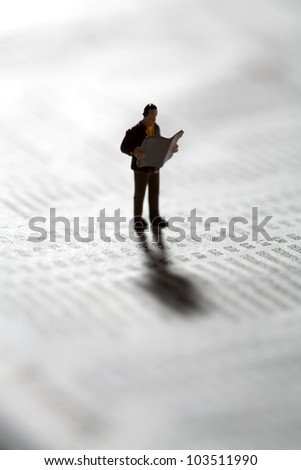 Tiny miniature model of an investor checking market updates in the newspaper as he stands on a financial document