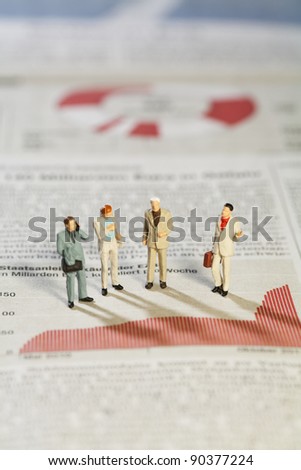 Business Strategy Meeting, four miniature models of businessmen standing above a bar graph as though in a meeting.