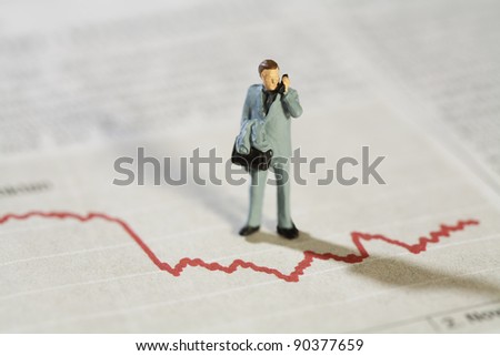 Analysing Business Statistics, a miniature model businessman stands over a red line graph talking on his mobile phone.