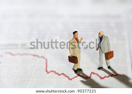 Businessmen in Conversation, two miniature models of businessmen in conversation standing over a red line graph .
