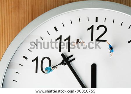 Countdown To Midnight And New Year. A team of miniature toy figurines tries to push the minute hand to midnight, closeup on a portion of a clock face.