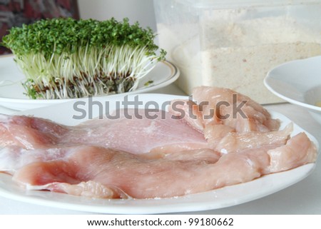 Raw chicken on plate with breadcrumbs, mixed eggs and cress.