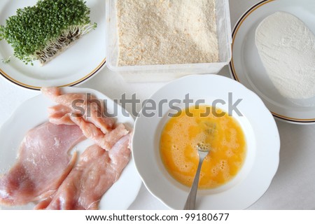 Raw chicken on plate with breadcrumbs, flour, mixed eggs and cress.