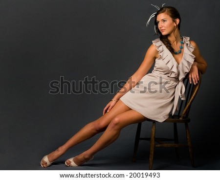 Pretty girl poses on a wooden chair against grey backdrop