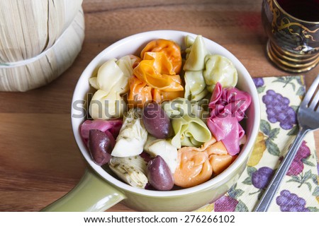 Colorful Italian pasta dish served with artichoke hearts and kalamata olives in a ceramic bowl, accompanied by a glass of Chianti wine for dinner or lunch