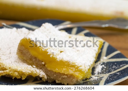 Lemon Bar serving freshly backed and covered in powdered sugar.  Served on a blue and white plate