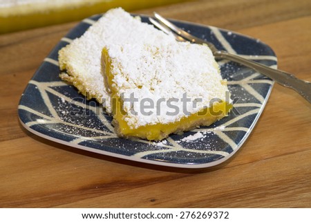 Lemon Bar serving freshly backed and covered in powdered sugar.  Served on a blue and white plate