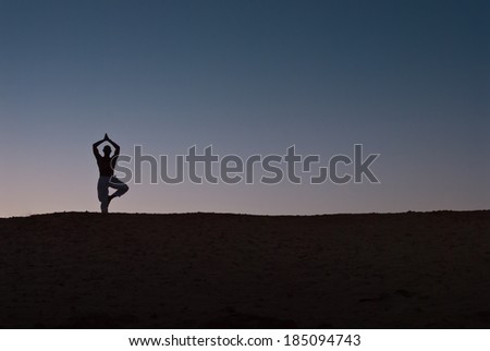 A male model practices yoga in the desert and is silhouetted against the sunset