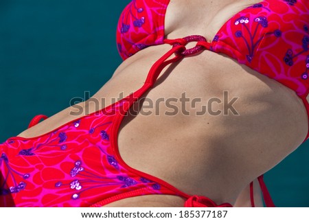 A slim woman in a pink bikini posing next to the ocean