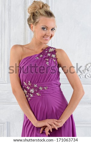 Beautiful blonde woman in lilac long dress in white interior.