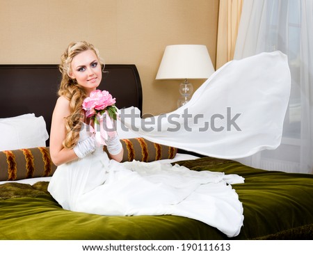 Beautiful woman in a wedding dress. She is in the bedroom with luxurious interior