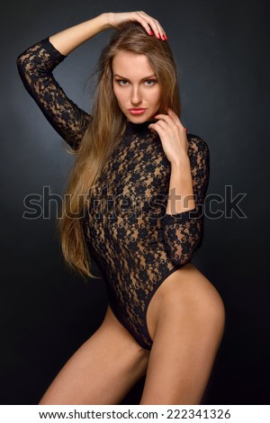 Beautiful woman with long hair in black lace lingerie, semi-dress posing in studio.