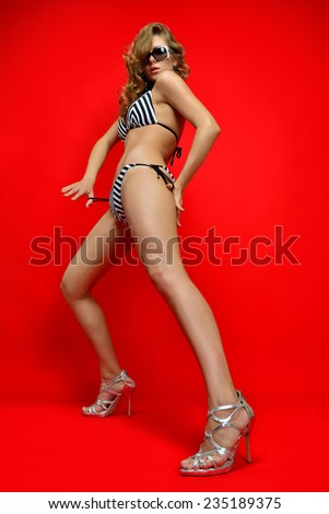Portrait of the beautiful blonde woman in a striped swimwear and sun glasses. Studio with red background.