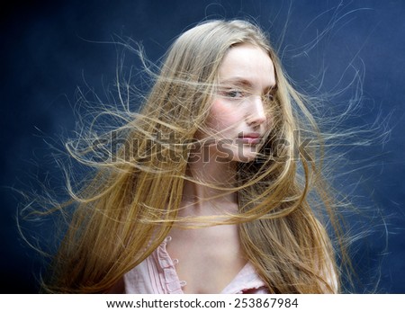 Portrait of the beautiful blonde woman with flying long hair. She is in studio .