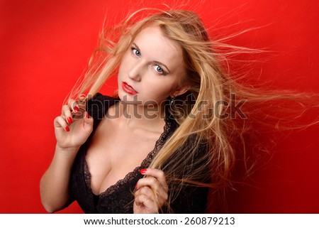 Portrait of the beautiful blonde woman with long flying hair. She dressed in black dress with breast  in studio with red background.