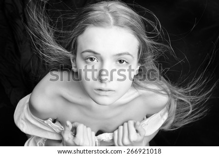 Portrait of the beautiful blonde woman with flying long hair. She is with naked shoulders  in studio . Monochrome image