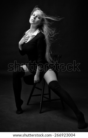 Beautiful woman in a black dress and stockings posing on the chair in studio with dark background .