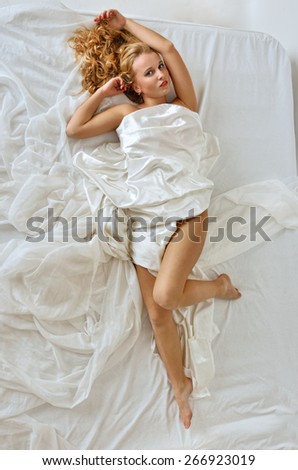 Beautiful blonde naked woman laying on white bed. View from above.