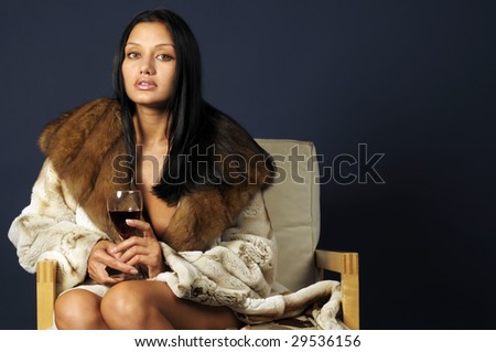Portrait of the beautiful woman with glass of wine. She dressed in fur coat