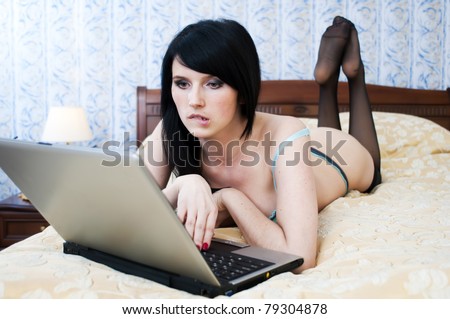 Portrait of the beautiful woman with laptop. She is lying on the bad in underwear.