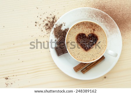 Cappuccino cup with heart shape on foam with chocolate, cacao, and cinnamon