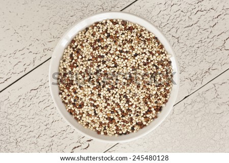 Tri-color Quinoa in small white dish photographed from above on diagonal cream colored and red craquelure background.