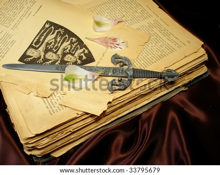 age-old book with a white petals and dagger and arms on yellow pages