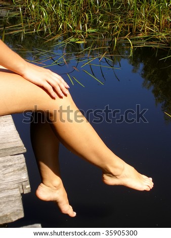 tan legs dangling in front of a beautiful dark blue lake