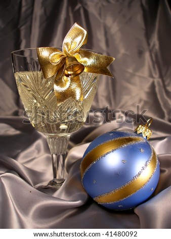Glass of champagne with a gold bluebell and Christmas decoration on a background light silk drapery