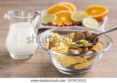 Healthy breakfast with jug of milk, corn flakes an fruits on the brown table.
