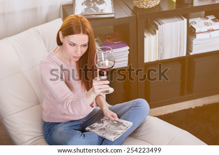 Woman read a book and drinking red wine on the sofa in the room.