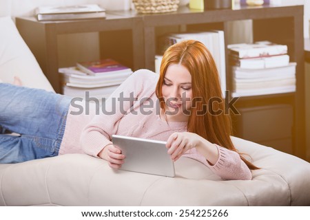 Thin girl read the tablet on the sofa in the room.
