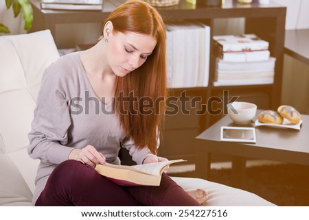 Thin young girl read a book on the sofa in the room.