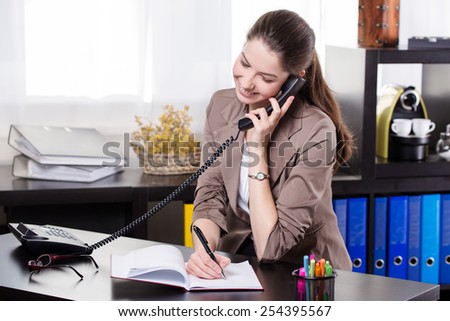 Elegant business woman talking on land line telephone and write on the notes in the office.