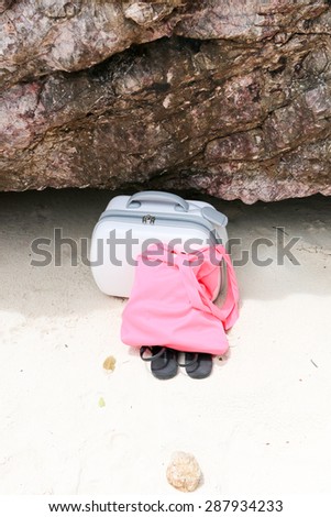 Suitcase, cloth bag and sandal left on sand