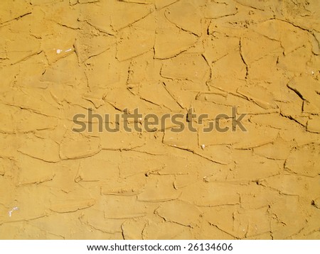 Rough textured concrete or stucco exterior wall painted a gold color.