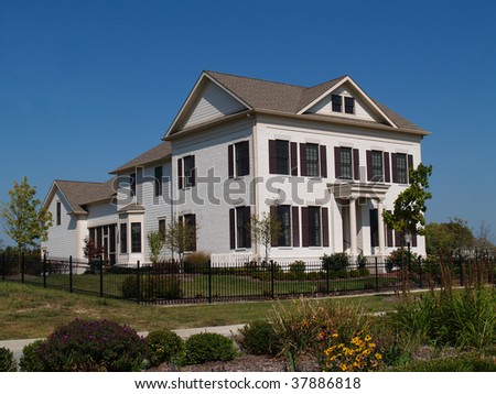 Two story new home built to look like an old historical home complete with the added on look, painted brick and a wrought  iron fence.